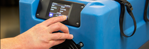 Hand operating the control screen on a blue dehumidifier.