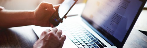 Person using a laptop and smartphone at a desk.
